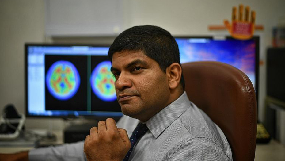  ​Associate Professor Nagaendran Kandiah in front of brain images showing harmful amyloid plaques that appear in red.ST PHOTO ARIFFIN JAMAR